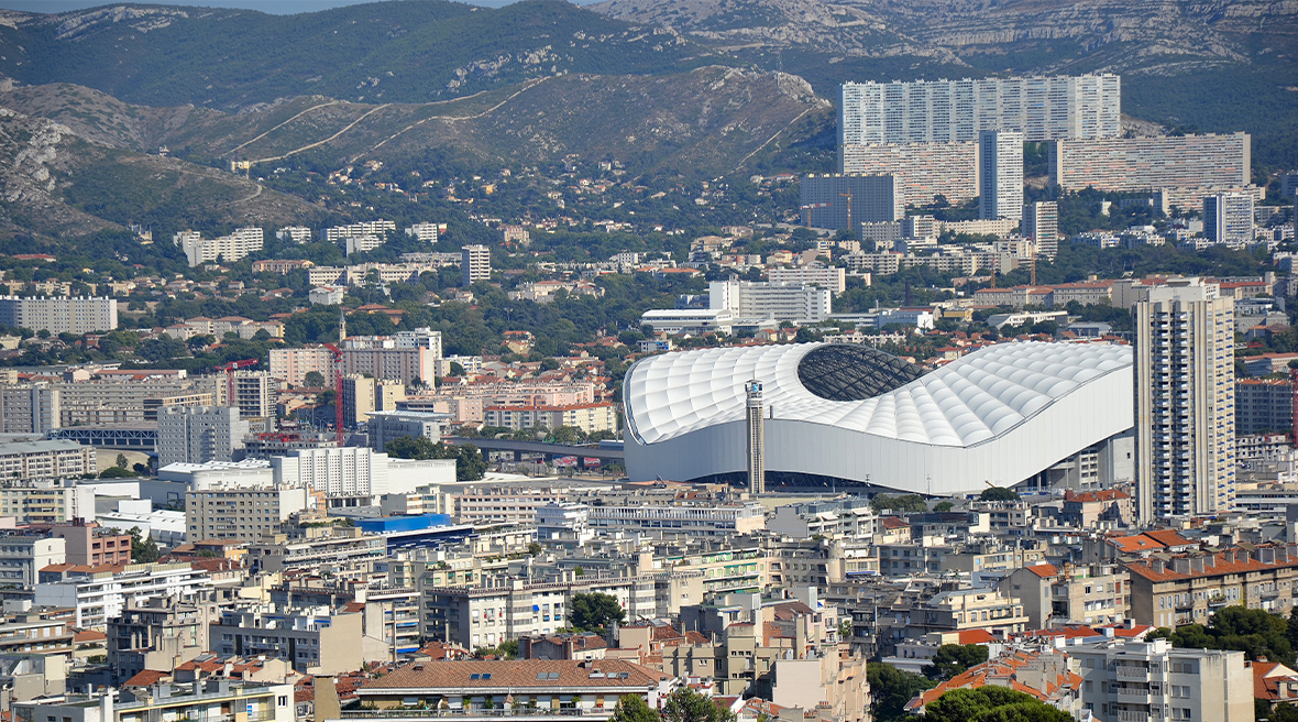A huge sports stadium is the main feature in a cityscape, with low level buildings and tower blocks around it in the foreground and background